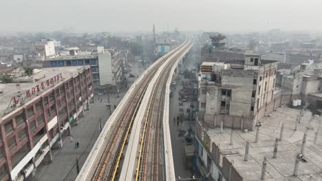 aerial parallax shot along empty orange metro railtrack in lahore with hazy air pollution seen in background