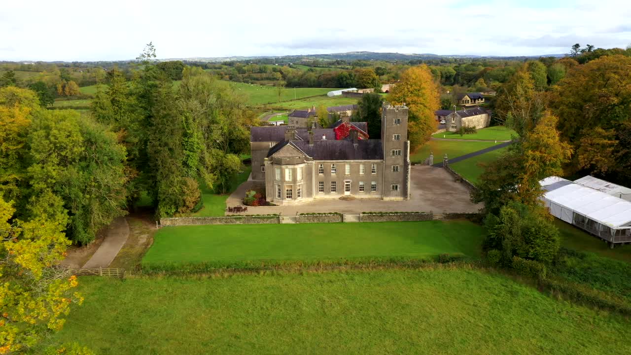 Aerial tracking left reveal of castle grounds with vibrant fall foliage and winding driveway in golden sunlight, Belle Isle Castle