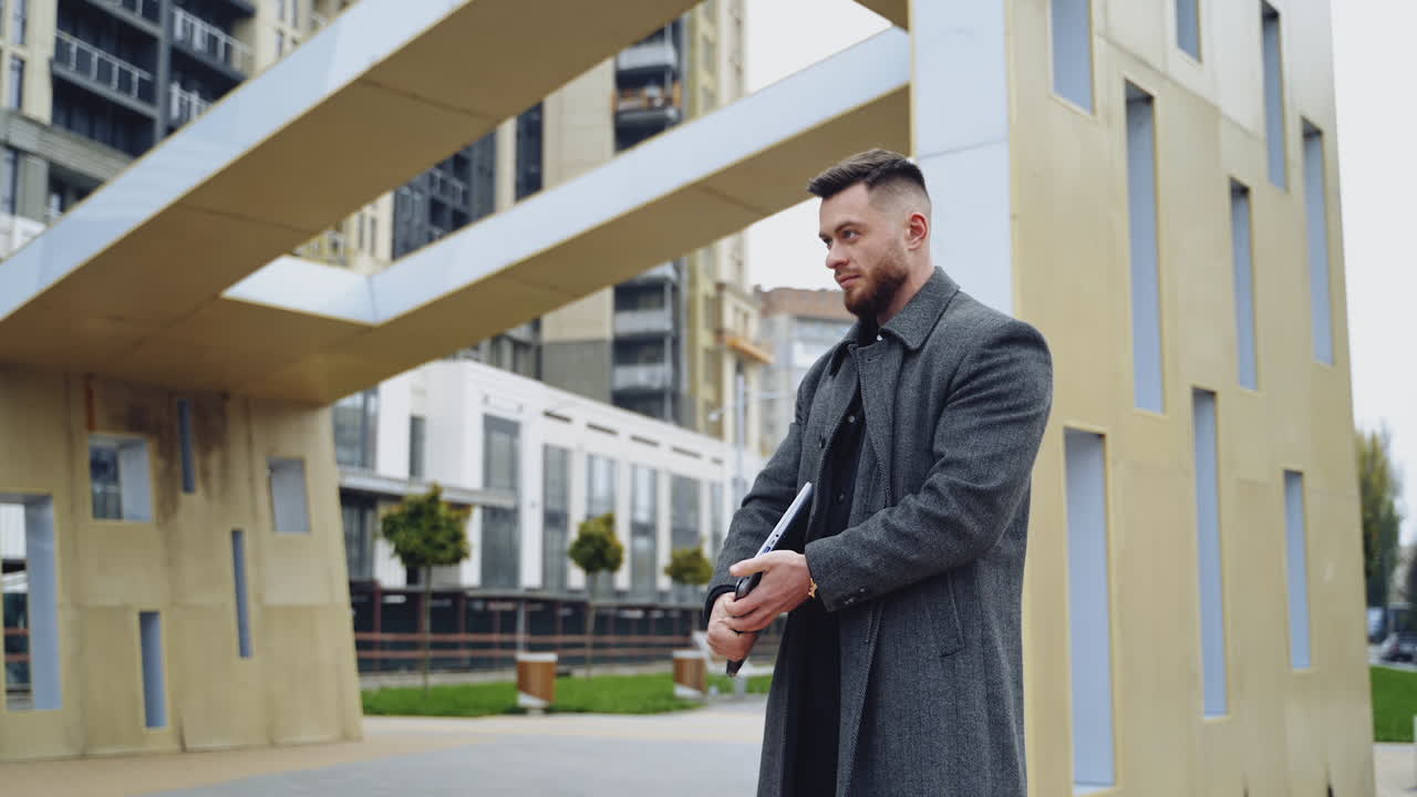 Businessman with a laptop outdoors. Handsome man in a coat working on wireless computer in the city street. Business concept.