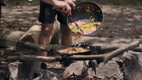 Agregar-Verduras-En-Una-Sartén-De-Hierro-Fundido-Debajo-De-Una-Fogata-En-Pulau-Ubin,-Singapur---Cerrar