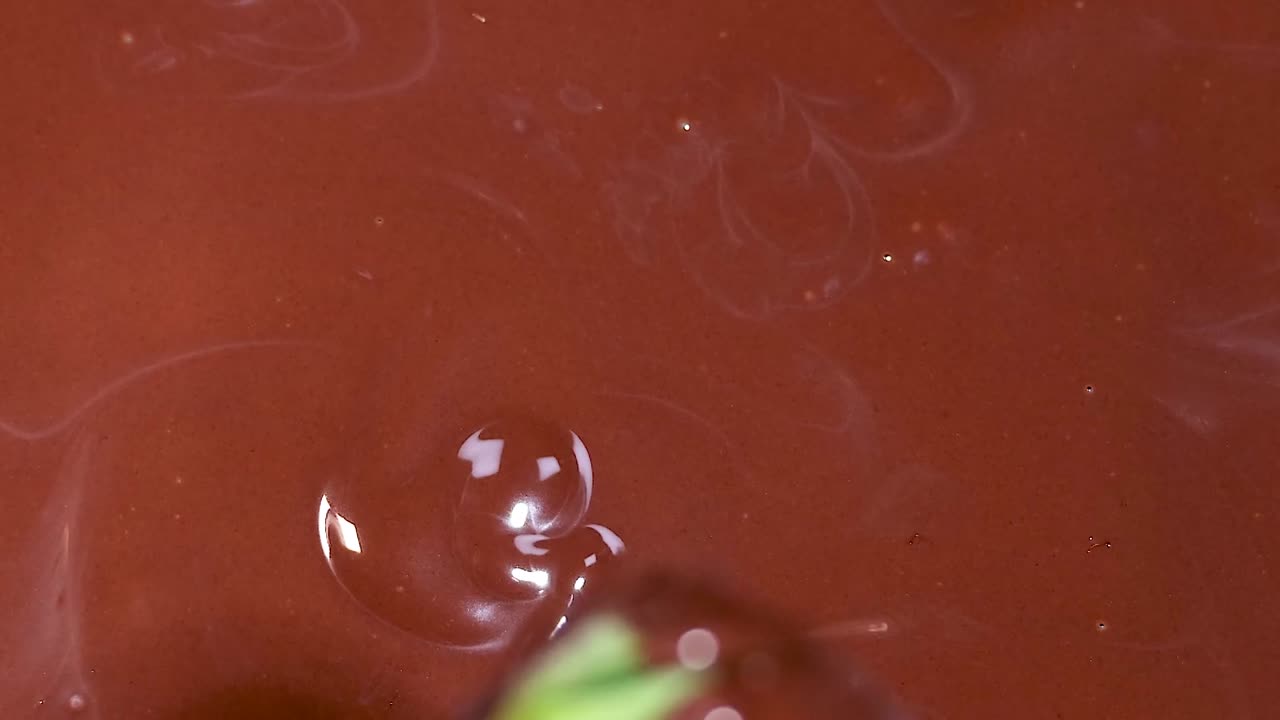 Una fragola viene immersa e sollevata da una pozza di cioccolato lucido, evidenziando la ricca consistenza e i colori vivaci.