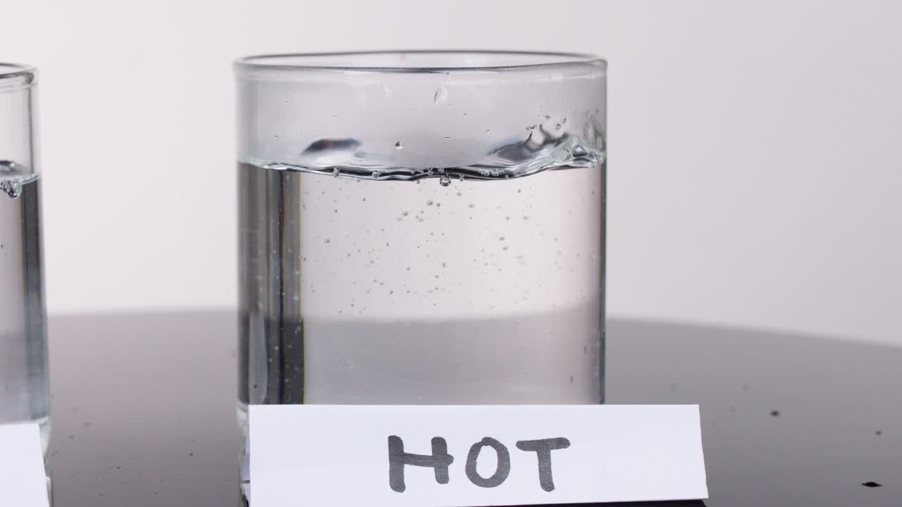 Clear water poured into glass labeled hot, bubbles form, studio lighting, static camera, scientific context
