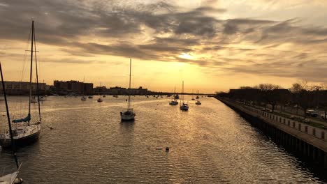 Ein-Schuss-Aus-Geringer-Höhe-über-Der-Bucht-Von-Sheepshead-Während-Eines-Goldenen-Sonnenaufgangs-Mit-Im-Wasser-Verankerten-Booten