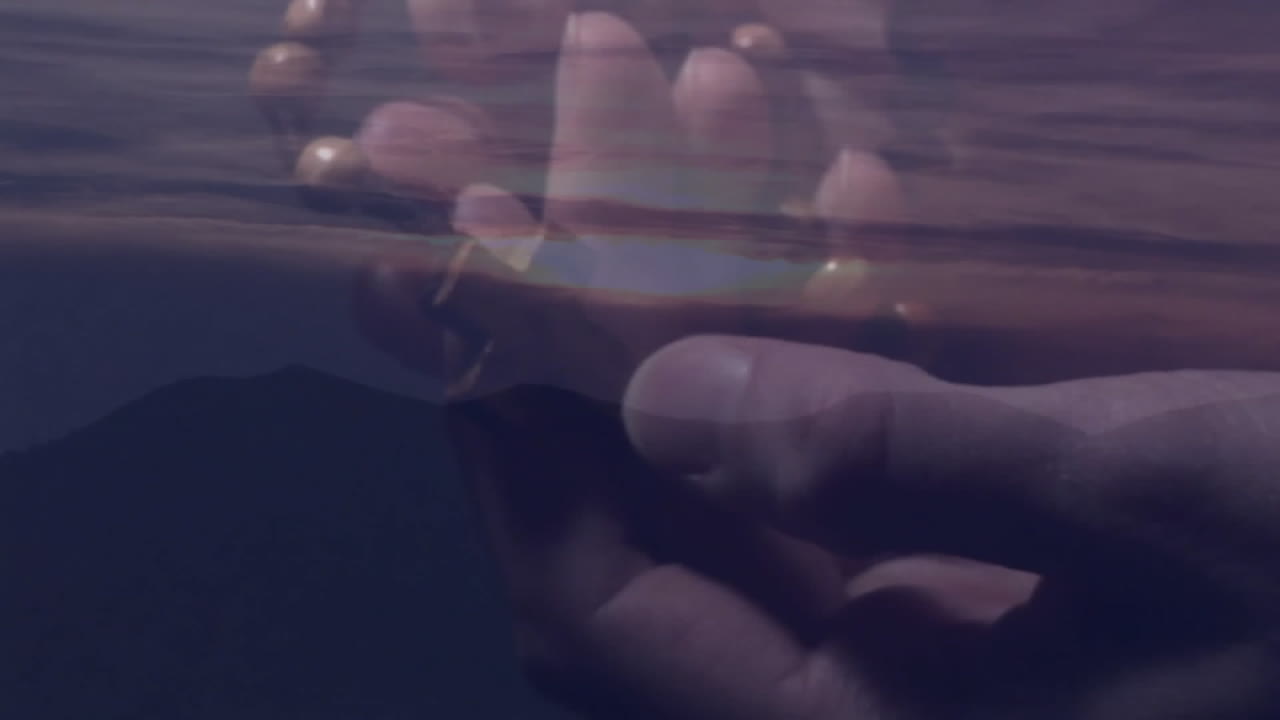 Holding prayer beads over serene landscape at dusk, hands creating animation effect