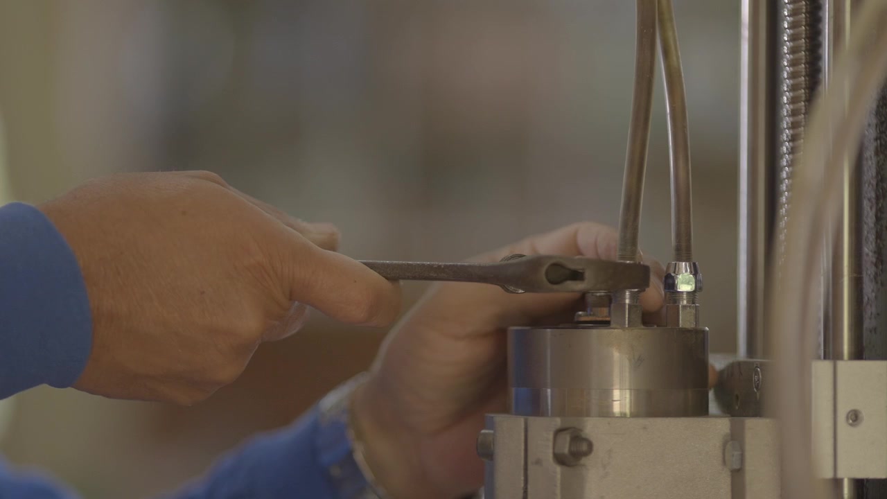 Hand adjusting tubing mechanism, close up detail, industrial scientific setting, focus on precision and intricate work.