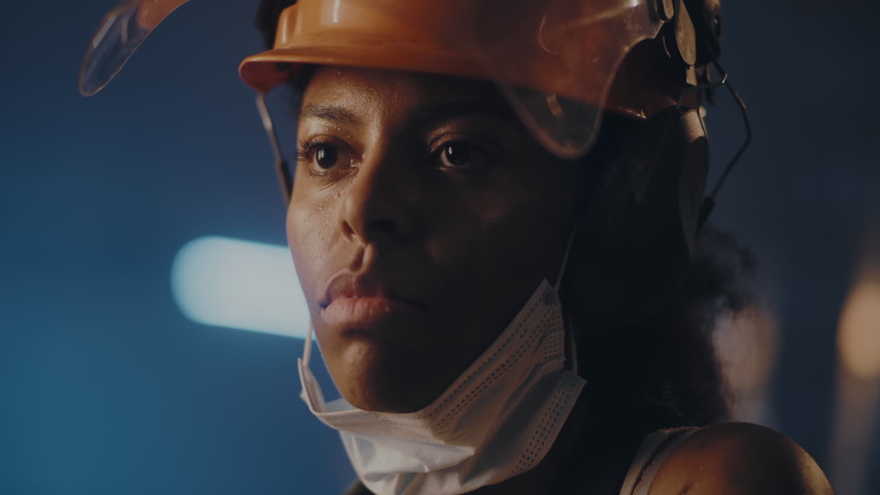 exhausted Female Factory Worker Removing her Hardhat after a Long Shift a Weary Young Woman in a Gray and Yellow Work Uniform Removes her Hardhat her Expression Reflecting the Weight of a Demanding Day in the Bustling Factory the Scene Captures the Essence of Hard Work and Resilience Showcasing the 