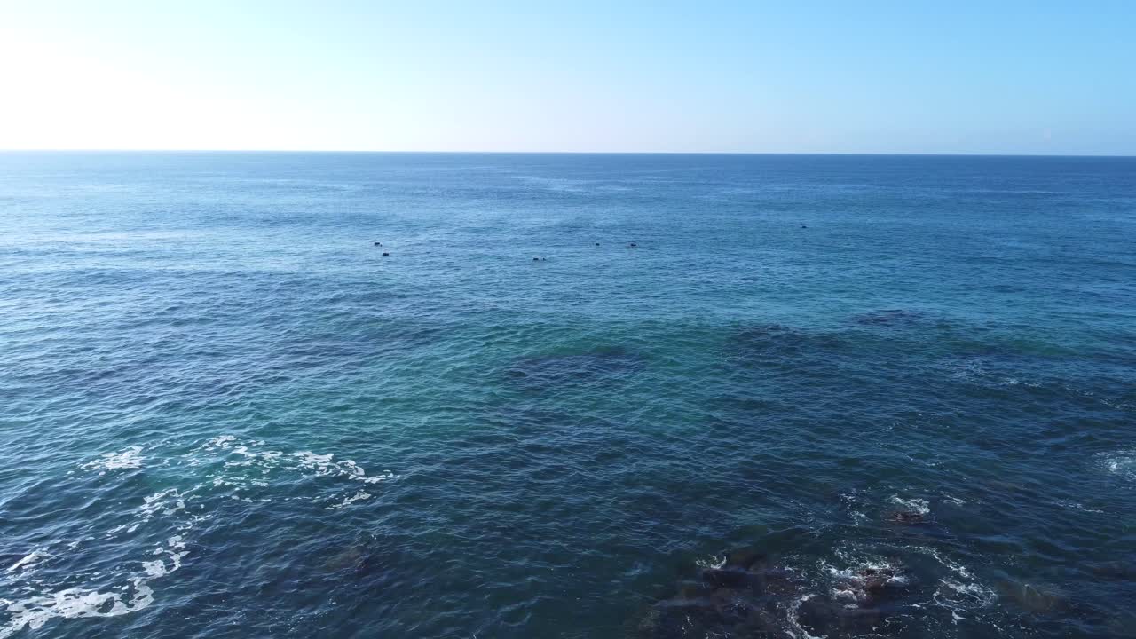 Smooth drone footage flying backwards from the open sea to the sandy shoreline, transitioning from a wide ocean horizon to detailed views of rocks and coastal textures in a cinematic movement.