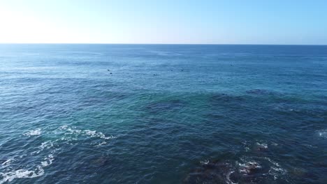 smooth drone footage flying backwards from the open sea to the sandy shoreline, transitioning from a wide ocean horizon to detailed views of rocks and coastal textures in a cinematic movement.
