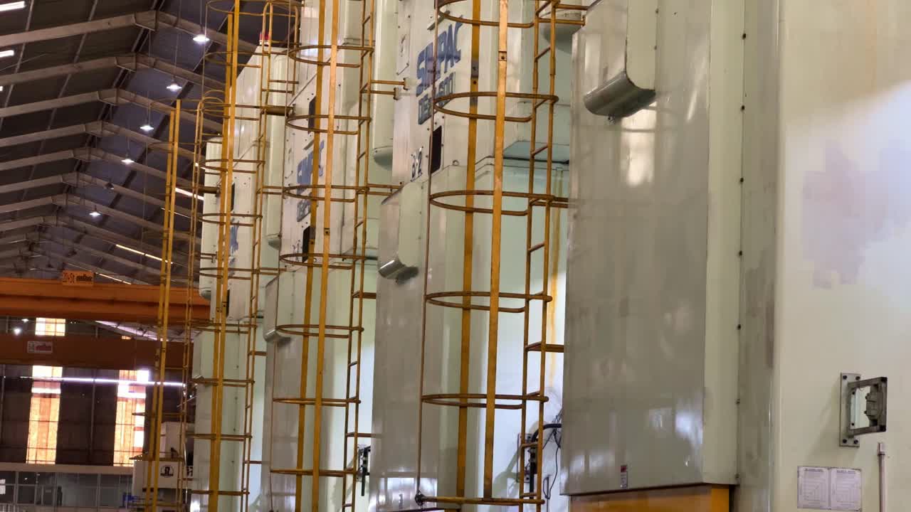 Industrial production plant with multiple vertical machines lined up, each fitted with protective yellow access ladders. Organized layout and heavy-duty infrastructure of a modern manufacturing plant