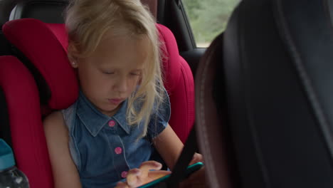 little girl playing on tablet in car seat