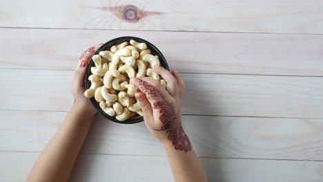 hands holding a bowl of cashews with henna