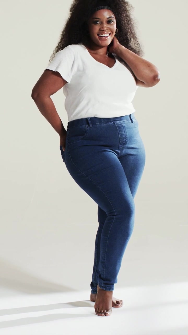 Video verticale: Una modella sorridente si muove mentre la telecamera riprende, spostandosi in studio, con maglietta bianca e jeans.