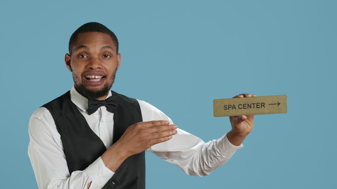 empleado del hotel en tuxedo señalando a la gente al centro de spa usando un letrero en la pared