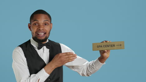 hotel employee in tuxedo pointing people to the spa center using a wall sign