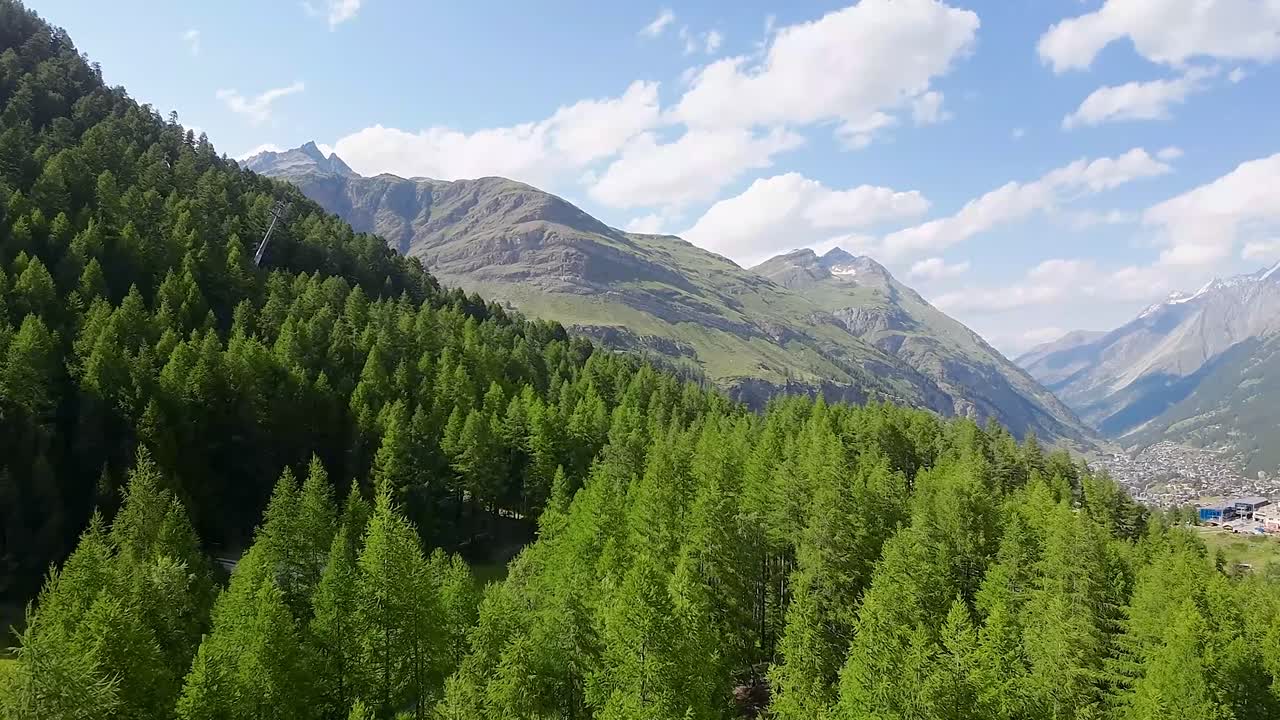 vuelo sobre un bosque en las hermosas montañas de los alpes suizos con la ciudad de zermatt en el fondo
