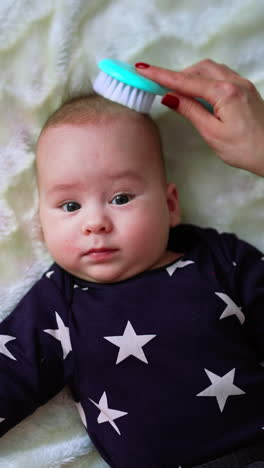 mommy is brushing thin baby hair. little adorable boy enjoying the process and looks at his mum lovingly. top view. white backdrop. vertical video