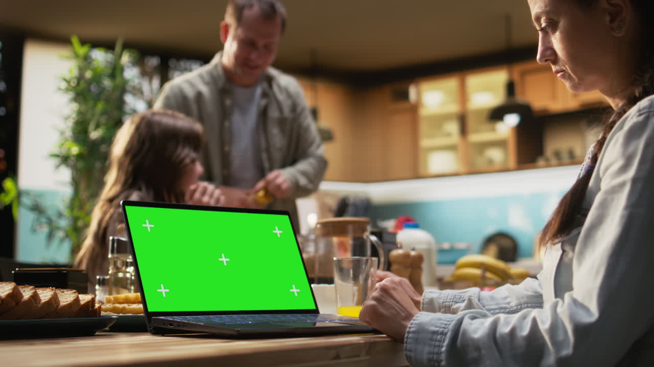 Green screen laptop next to family enjoying relaxing weekend breakfast