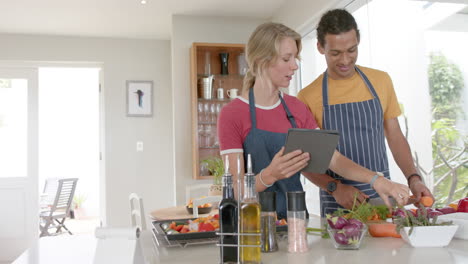 pareja feliz preparando verduras frescas y usando tableta en la cocina, cámara lenta