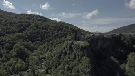 Drone's-panoramic-video-showcases-the-breathtaking-beauty-of-Castellfollit-de-la-Roca,-Spain:-medieval-village-perched-atop-a-striking-volcanic-cliff