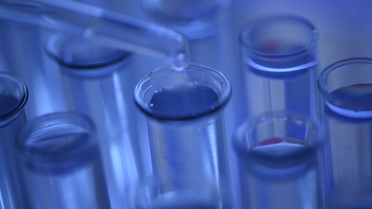 Pipetta illuminata di blu che rilascia liquido in una provetta in laboratorio