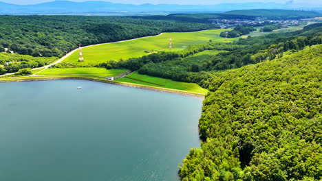 Peaceful lake surrounded by the forests and big meadow. Electrical transmission towers are in the field. Aerial view.