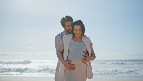 expectant parents standing ocean beach at sunlight. couple enjoying pregnancy