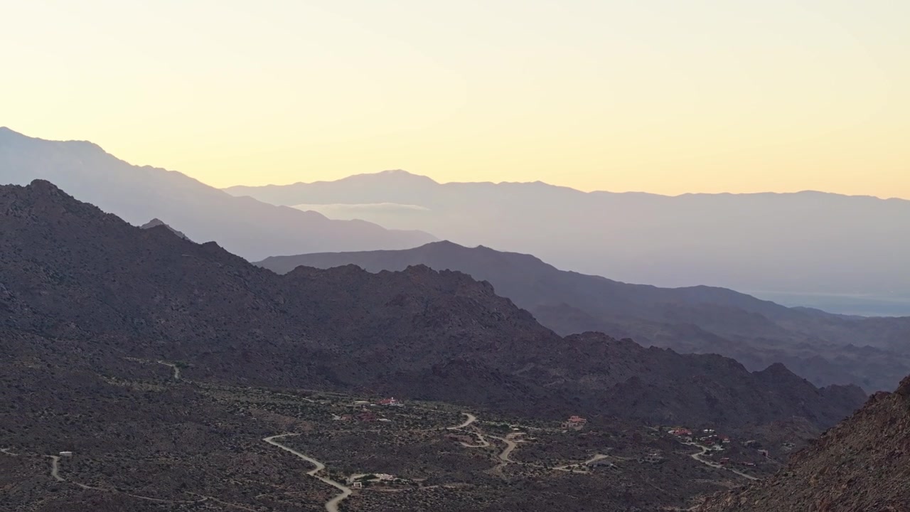 Creste montuose aspre di Palm Springs che si affacciano su una valle desertica sotto una morbida luce dorata, panoramica aerea con drone.