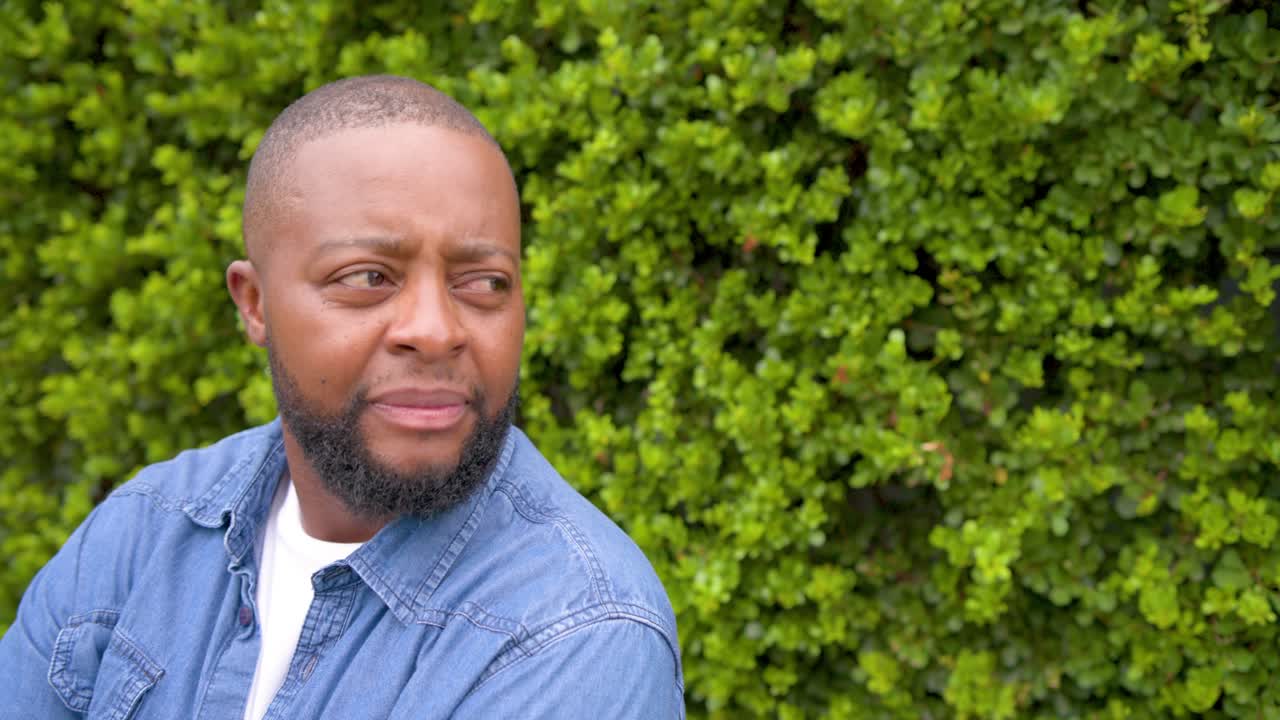 Homme africain adulte, assis à gauche près d'une haie en T-shirt blanc, se tournant vers un signal hors champ en riant, avec espace pour le texte