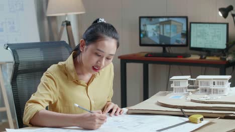 asian woman engineer with a laptop looking at blueprint while working at the office