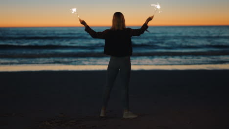 mujer bailando con bengalas en la playa al atardecer celebrando la víspera de año nuevo niña divirtiéndose bailando con fuegos artificiales disfrutando de la celebración del día de la independencia junto al mar