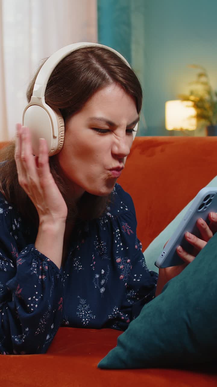 joven con auriculares inalámbricos relajándose en el sofá en casa usando un teléfono inteligente escuchando música