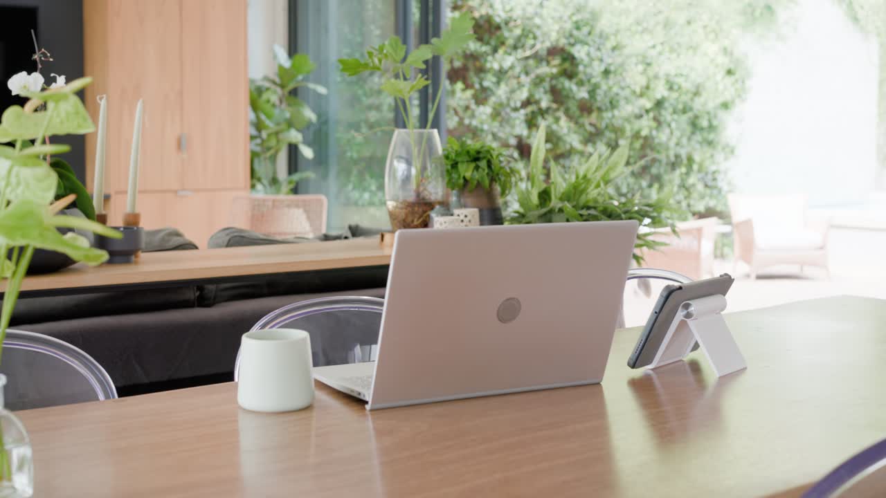 Camera is panning right and forward, centering silver laptop on table, revealing garden via doors