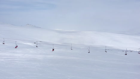 aerial view drone tracking following skiers in ski lifts heading to mountain peak on ski resort panning left kaimaktsalan greece