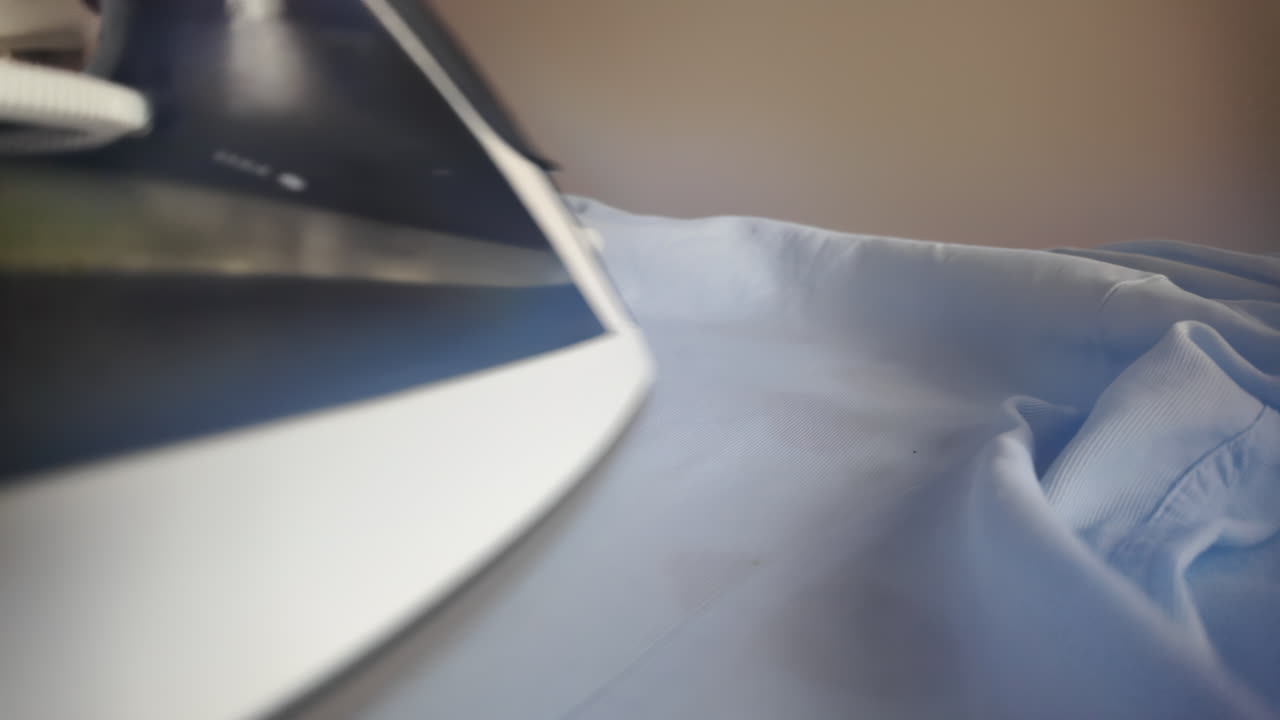 Close up woman ironing a blue shirt at home with white steam