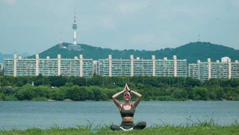 woman doing yoga meditation outdoors in a han river park of seoul, lotus and prayer hands above head for exercise, holistic wellness and stretching