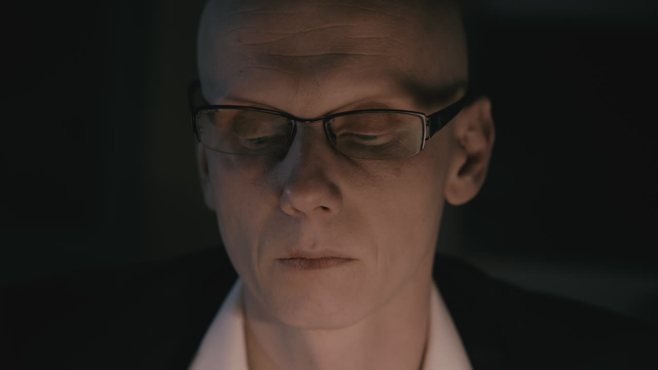 Pale bald accountant looks through the tax papers in the weird room at night