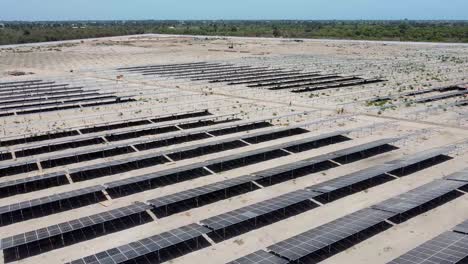dolly aéreo hacia adelante sobre paneles polvorientos en el sitio del proyecto solar fotovoltaico de jambur bajo construcción que muestra a los trabajadores cavando trincheras de cable