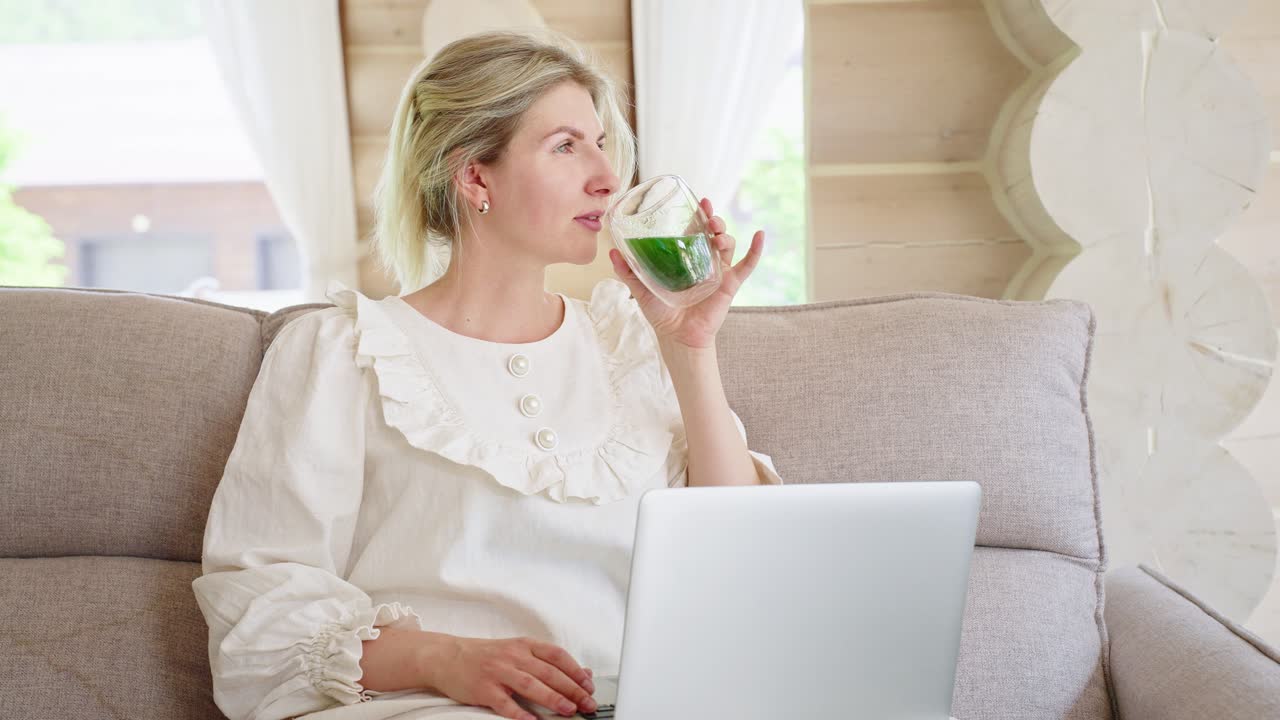 Woman Working on Laptop and Drinking a Green Smoothie