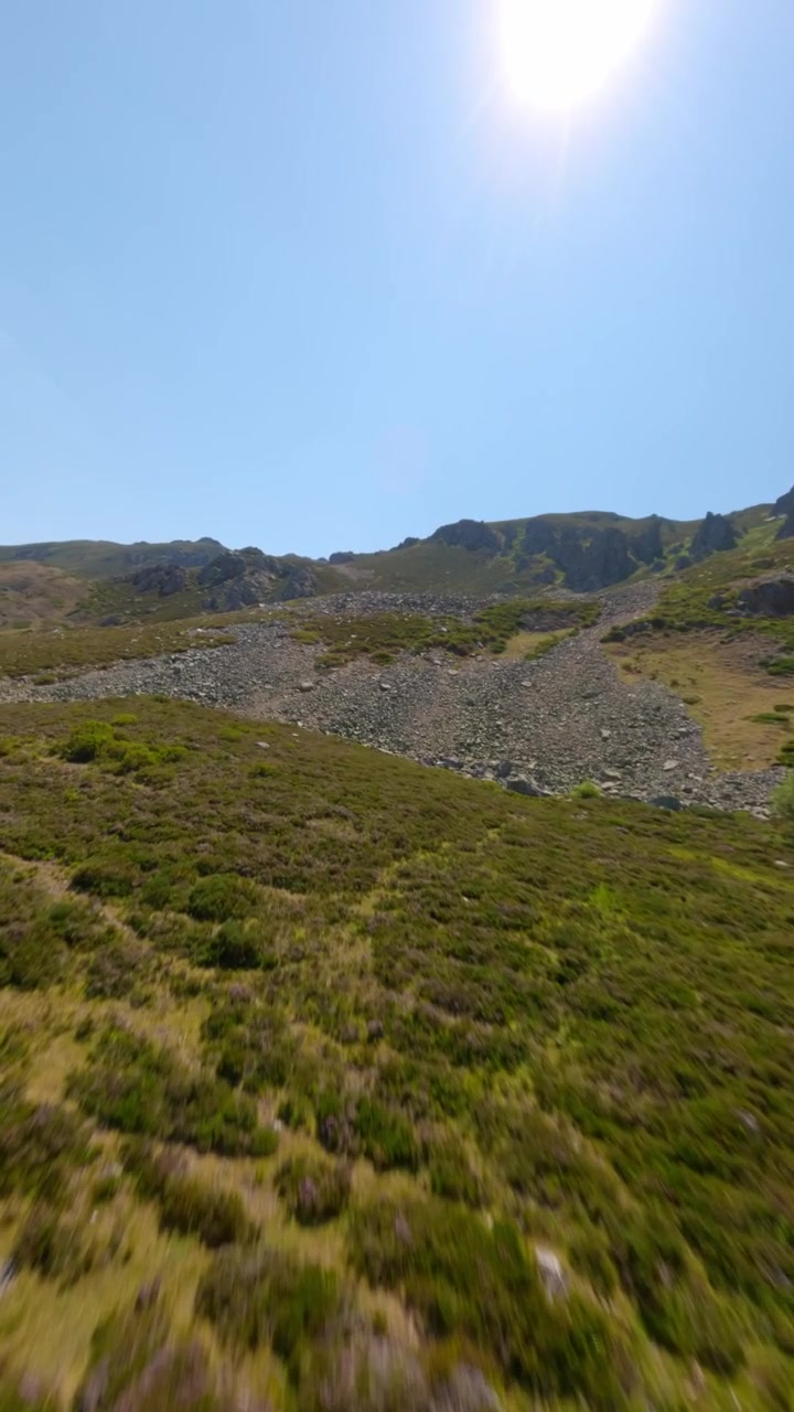 Volo dinamico verticale con drone FPV sopra cime rocciose illuminate dal sole e pendii scoscesi di Puerto San Isidro, Asturie, Spagna