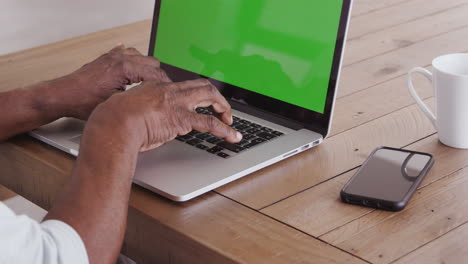 the hands of a senior black man sitting at a wooden table typing on a laptop computer, close up