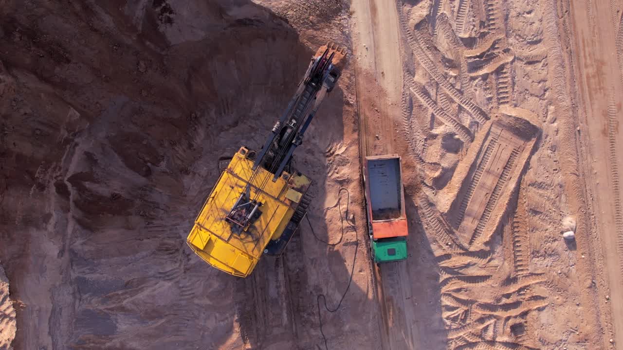 Electric rope shovel on sand mining in opencast. Mining excavator dropping rock ore into mine dump truck.