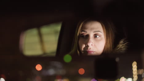 first-person view of a woman adjusting the car mirror at night, with her face clearly reflected in the mirror. the blurred city lights add a dreamy atmosphere. shot with a handheld camera