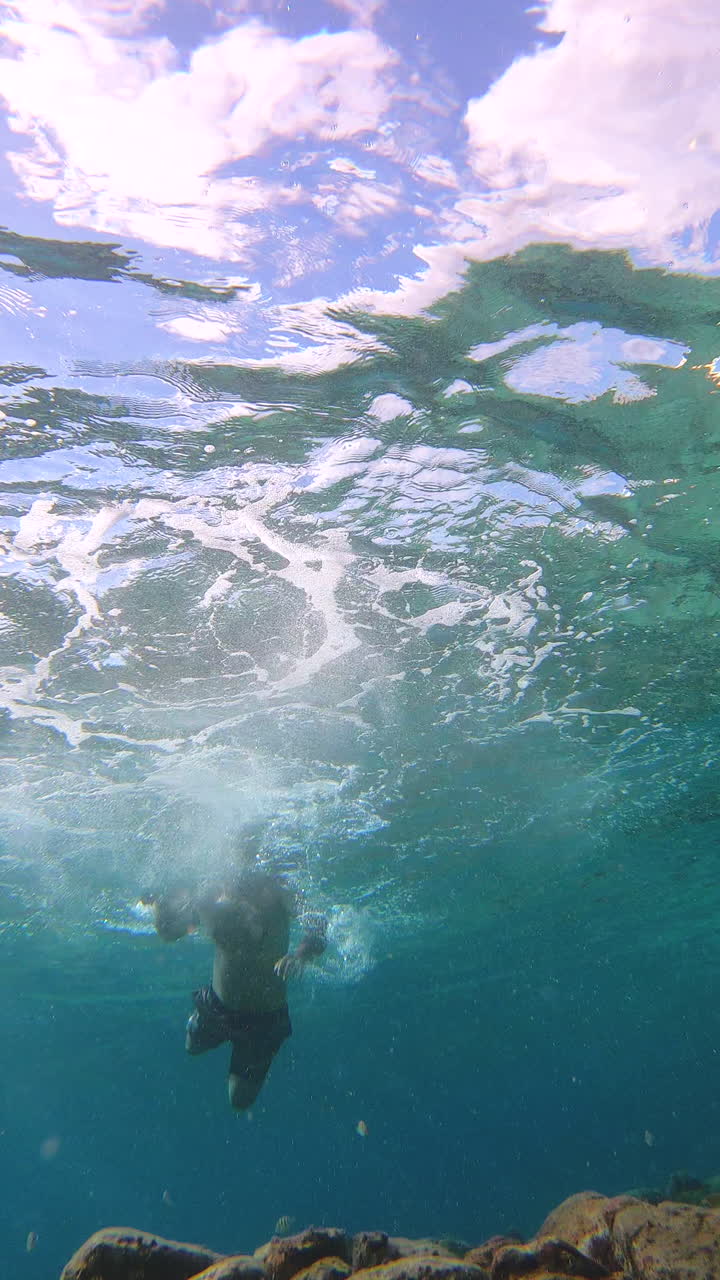 vertical slow motion shot of man diving shirtless in turquoise waters of Cozumel island, Caribbean sea, Mexico, enjoying summer vacation, creating bubbles and foam, water surface is visible above
