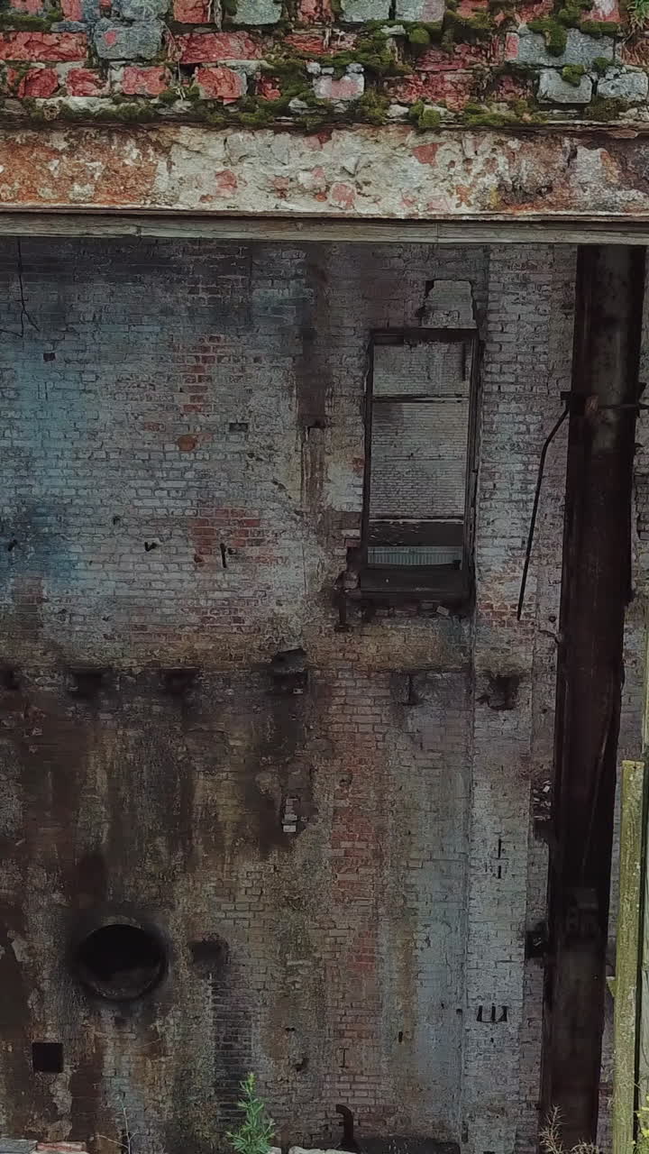 Flight over the destroyed factory. Facade of old industrial building for demolition, broken glass and destroyed frames. Vertical video