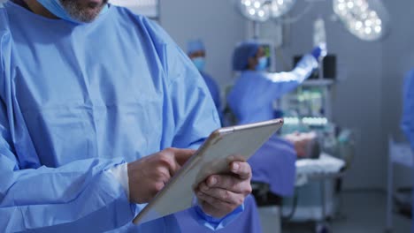 Portrait-of-caucasian-male-surgeon-standing-in-operating-theatre-using-tablet