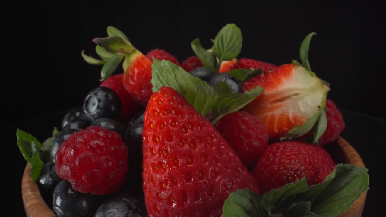 Macro view of forest fruits in a wooden bowl with black background, strawberries, blueberries and raspberries, healthy fruits, 4K shot