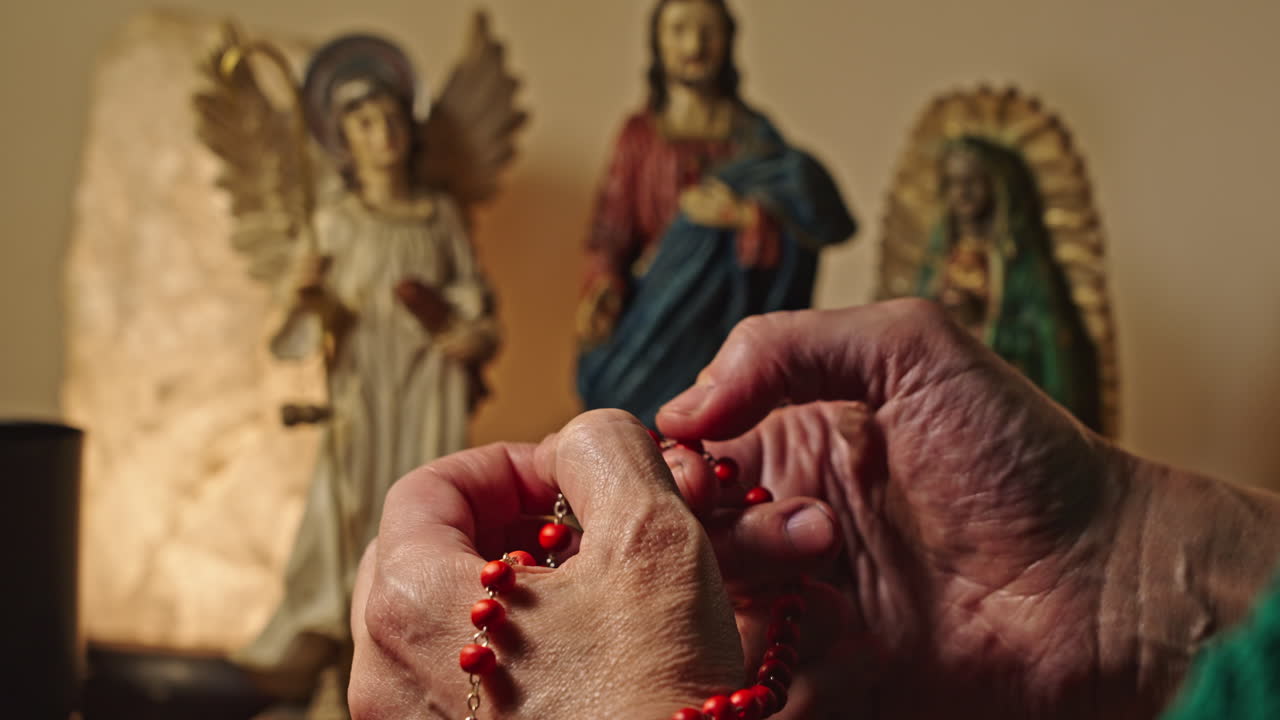 Primo piano di mani in preghiera con un rosario rosso