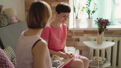 Two-woman-friends-talking-on-couch-and-knitting-needles-yarn