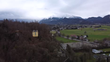 Cinematic-aerial-footage-of-the-country-side-of-Austria,-showcasing-a-19th-century-home-castle-in-the-foreground-and-snowy-mountains-in-the-background