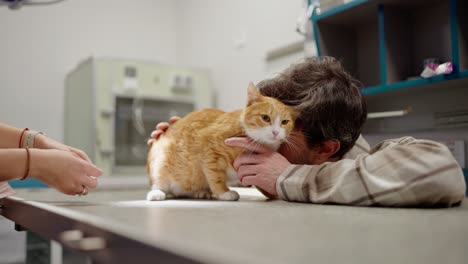 Close-up-a-brunette-guy-in-a-white-checkered-shirt-strokes-his-ginger-cat-together-with-a-girl-veterinarian-in-a-veterinary-clinic